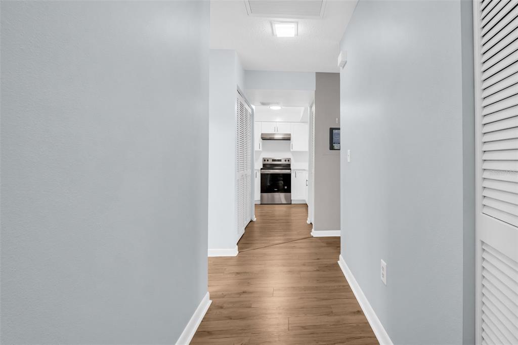 A hallway with light wood-look flooring leads to a kitchen with white cabinets and appliances — 2765 COUNTRYSIDE BOULEVARD UNIT 104, CLEARWATER, FL