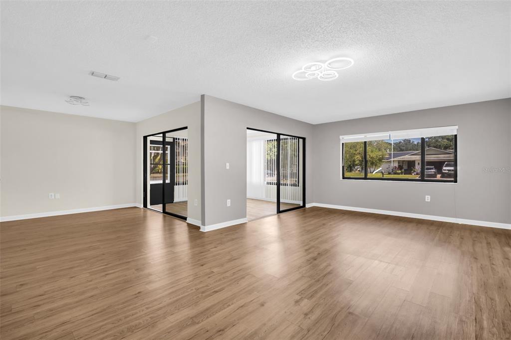 A spacious room with light wood-look flooring, gray walls, and black-framed glass sliding doors — 2765 COUNTRYSIDE BOULEVARD UNIT 104, CLEARWATER, FL