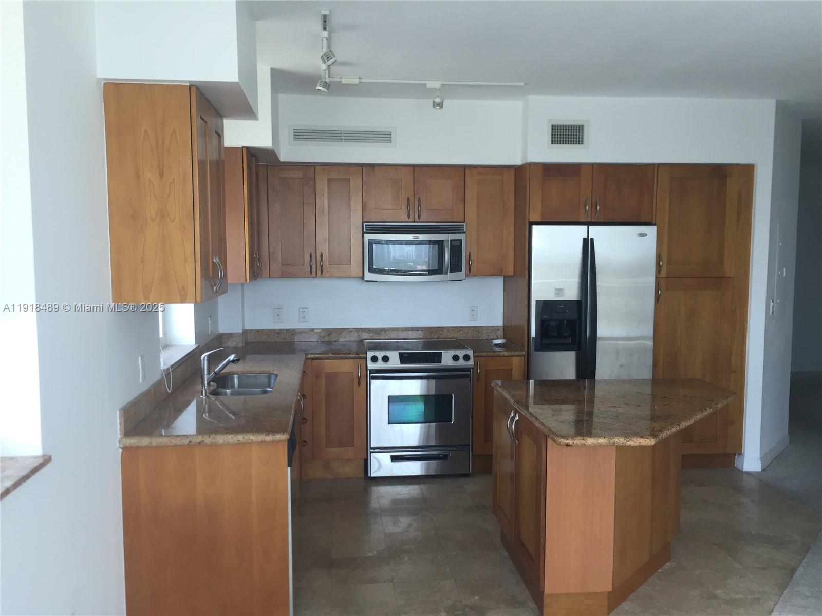 A kitchen features wood cabinets, granite countertops, stainless steel appliances, and a small island — 1745 E Hallandale Beach Blvd # 1807W, Hallandale Beach FL 33009, HALLANDALE BEACH, FL