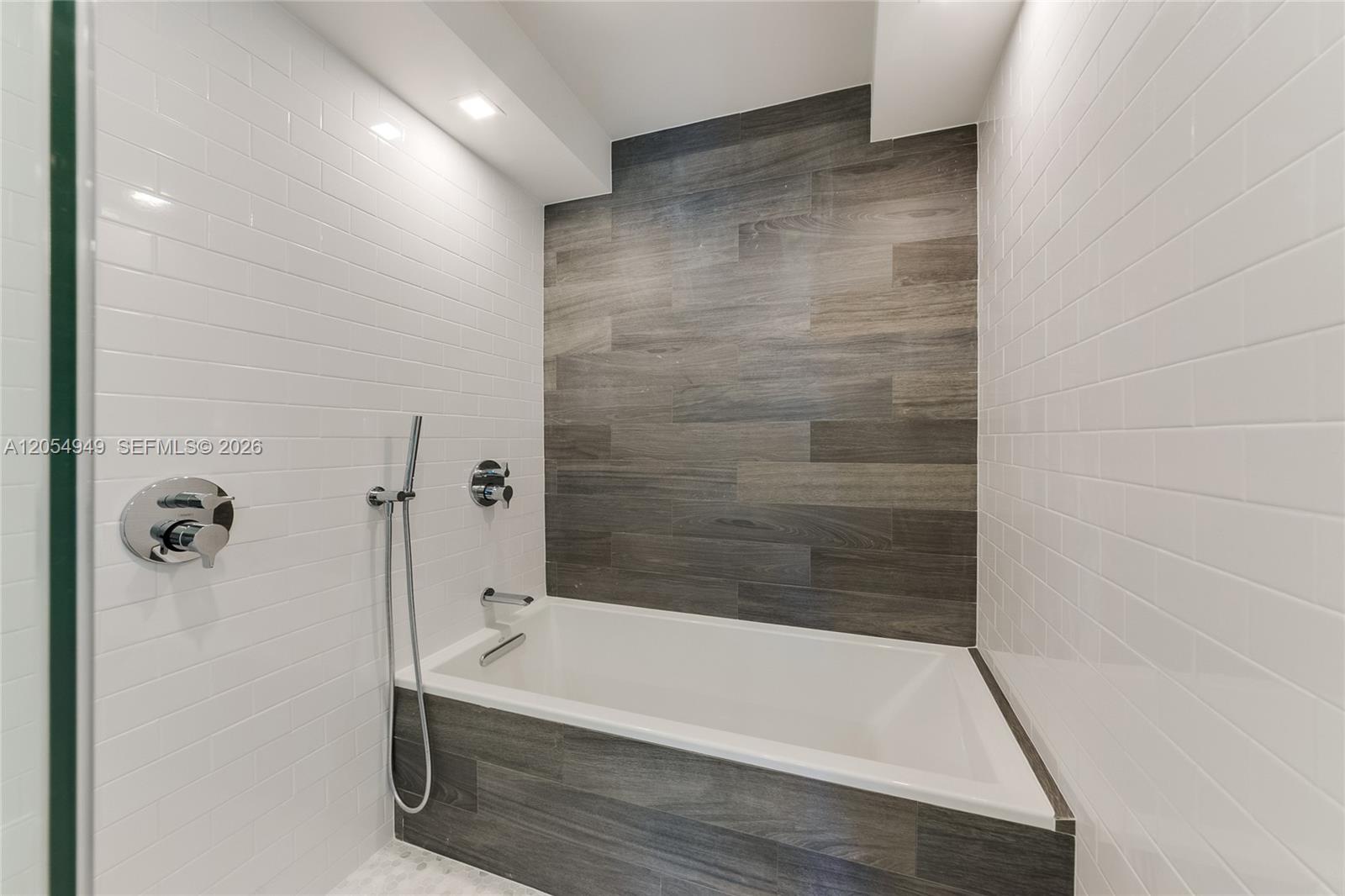 A bathroom features a white bathtub with wood-look tile surround and white subway tile walls — 11 Island Ave # 908, Miami Beach FL 33139, MIAMI BEACH, FL