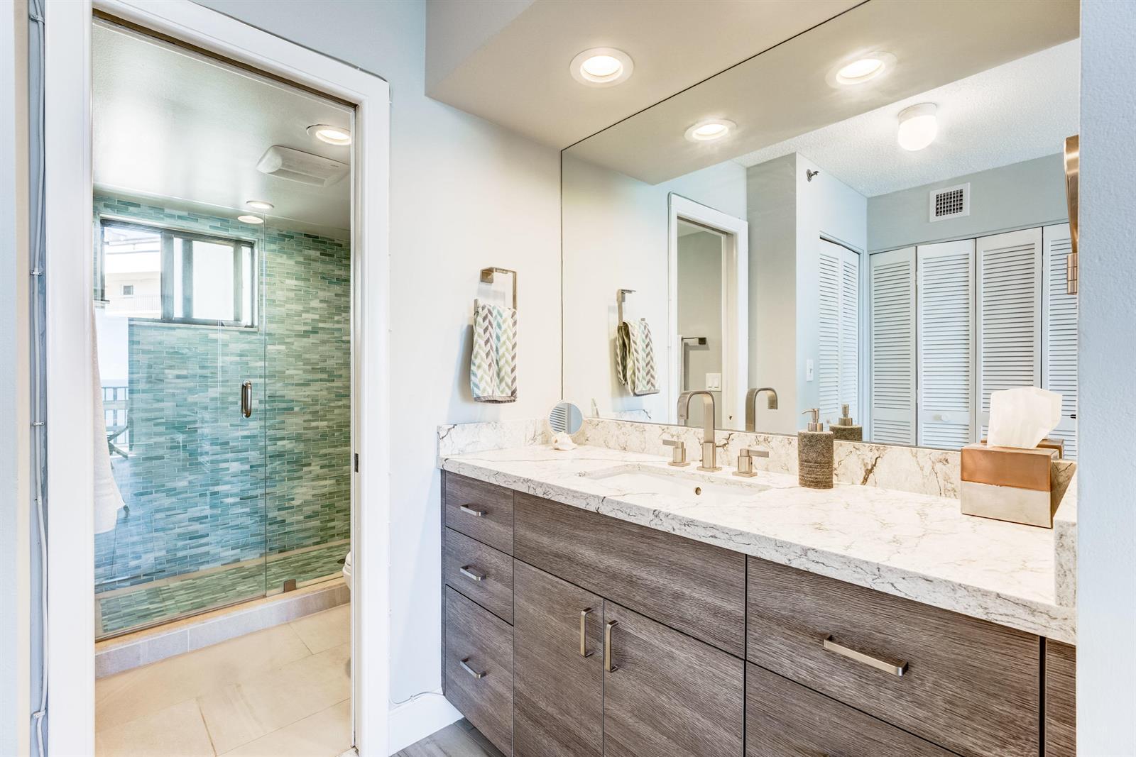 A bathroom features a wood vanity with a marble countertop and a glass-enclosed tiled shower — 200 Ocean Trail Way # 1107, Jupiter FL 33477, JUPITER, FL