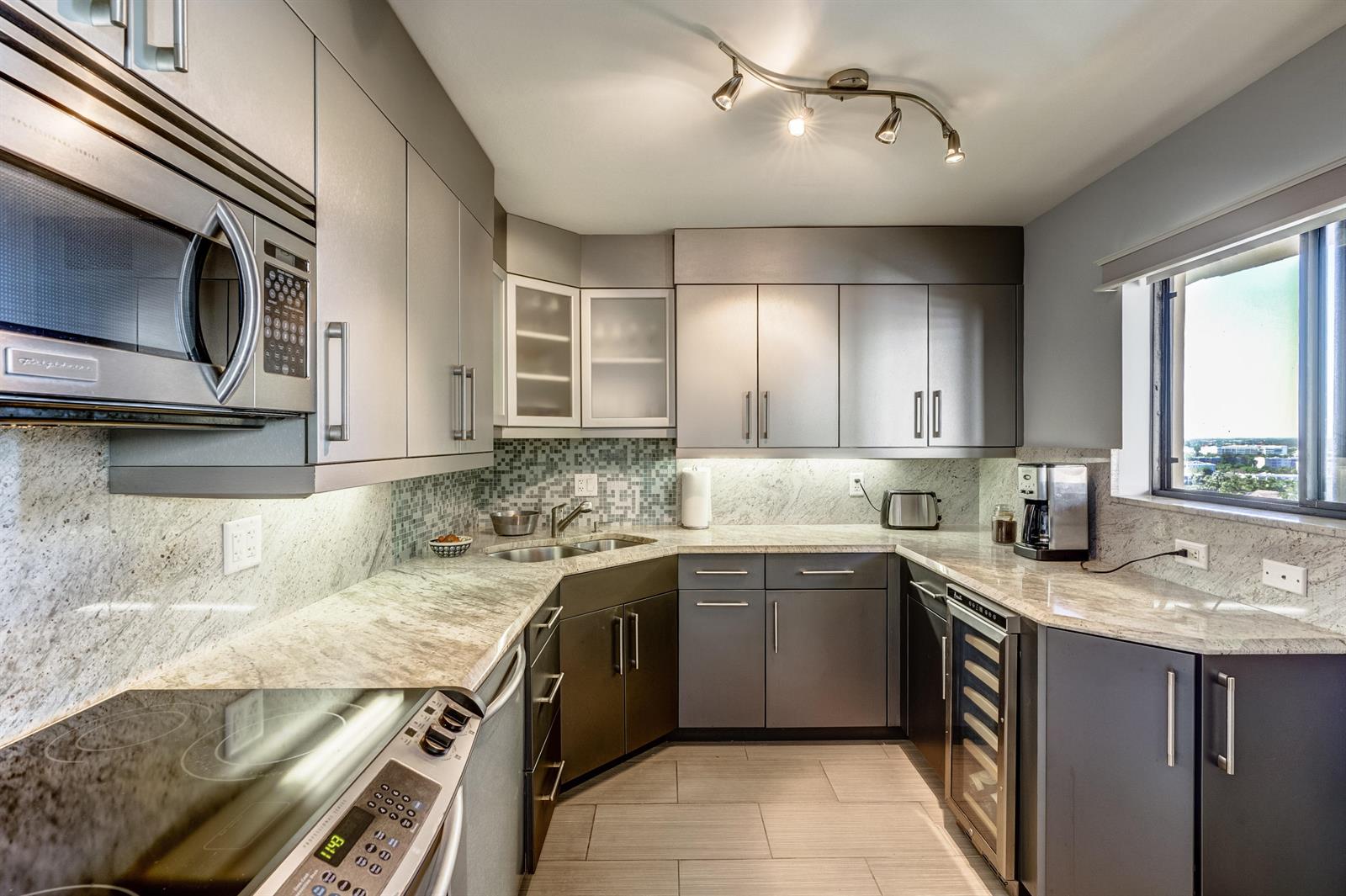 A modern kitchen features gray cabinets, granite countertops, stainless steel appliances, and a tile backsplash — 200 Ocean Trail Way # 1107, Jupiter FL 33477, JUPITER, FL