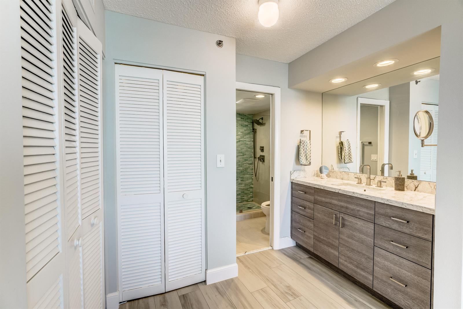 A bathroom features a wood-toned vanity with a stone countertop, louvered closet doors, and tile flooring — 200 Ocean Trail Way # 1107, Jupiter FL 33477, JUPITER, FL
