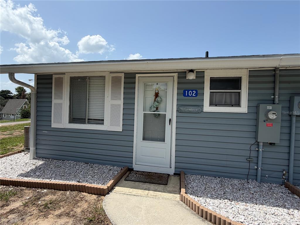 The exterior of a blue-sided house features a white front door, windows, and gravel landscaping — 10301 US HIGHWAY 27 UNIT 102, CLERMONT, FL