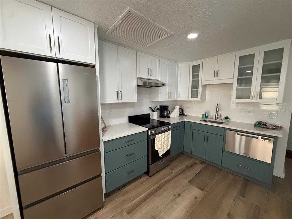 A kitchen features white upper cabinets, teal lower cabinets, stainless steel appliances, and wood flooring — 10301 US HIGHWAY 27 UNIT 102, CLERMONT, FL