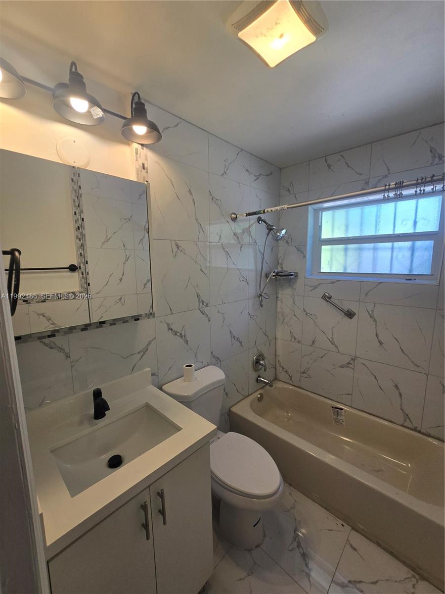 A bathroom features a vanity, toilet, and a bathtub with marble-patterned wall tiles — 6231 NE 1st Ave # 2, Miami FL 33138, MIAMI, FL