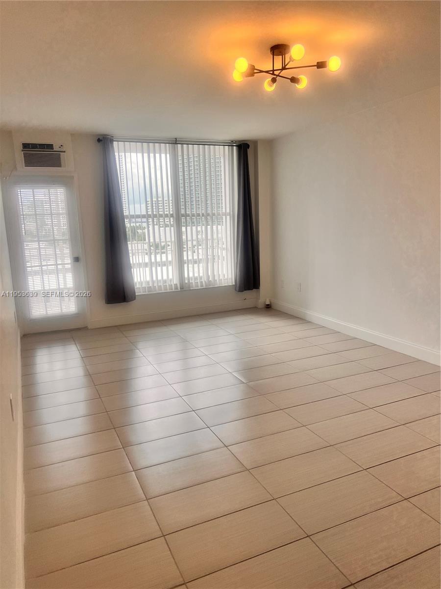 An empty room features light-colored tile flooring, a modern light fixture, and a sliding glass door — 1300 Lincoln Rd # B902, Miami Beach FL 33139, MIAMI BEACH, FL