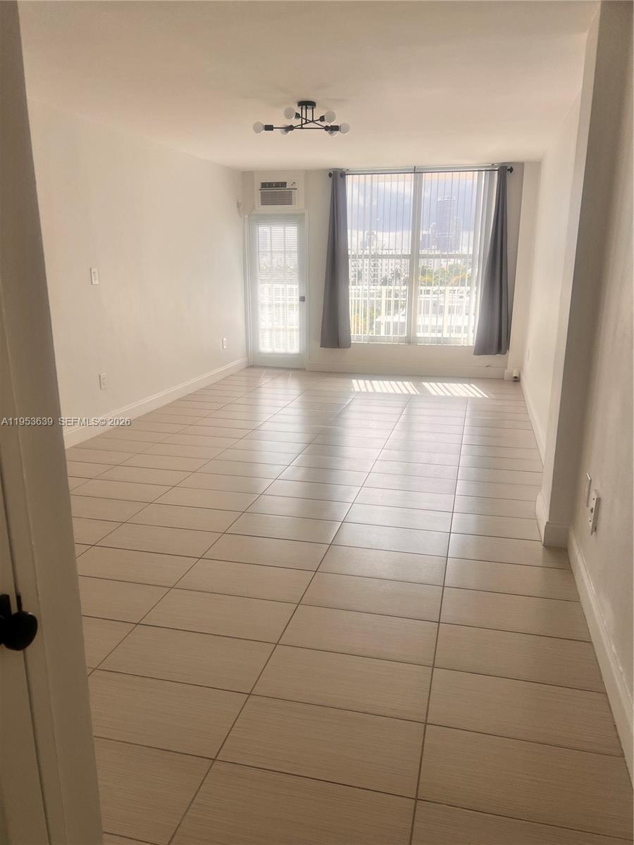 A bright living area features light-colored floor tiles, white walls, and a glass balcony door — 1300 Lincoln Rd # B902, Miami Beach FL 33139, MIAMI BEACH, FL