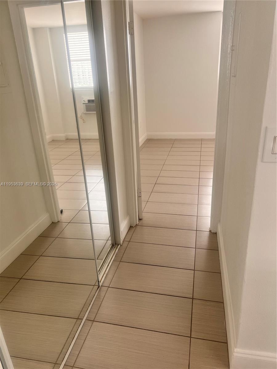 A hallway with light-colored tile flooring leads toward a room with a window air conditioner — 1300 Lincoln Rd # B902, Miami Beach FL 33139, MIAMI BEACH, FL