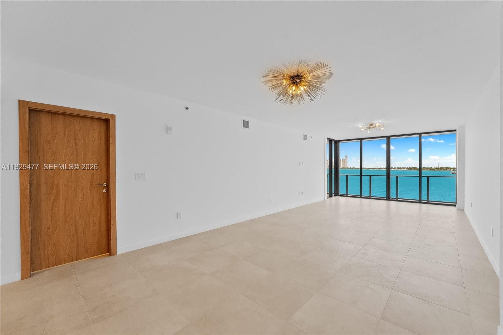 An empty room with light tile flooring, a wooden door, and floor-to-ceiling windows overlooking water — 1135 103 St # 403, Bay Harbor Islands FL 33154, BAY HARBOR ISLANDS, FL