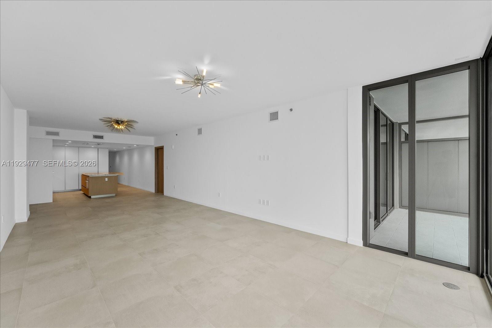 An empty living area features large light-colored floor tiles, white walls, and a glass balcony door — 1135 103 St # 403, Bay Harbor Islands FL 33154, BAY HARBOR ISLANDS, FL