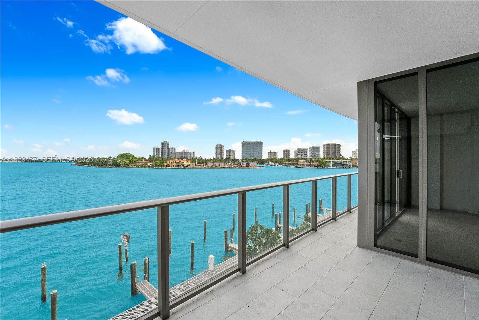 A balcony with a glass railing overlooks a bay with a distant city skyline — 1135 103 St # 403, Bay Harbor Islands FL 33154, BAY HARBOR ISLANDS, FL
