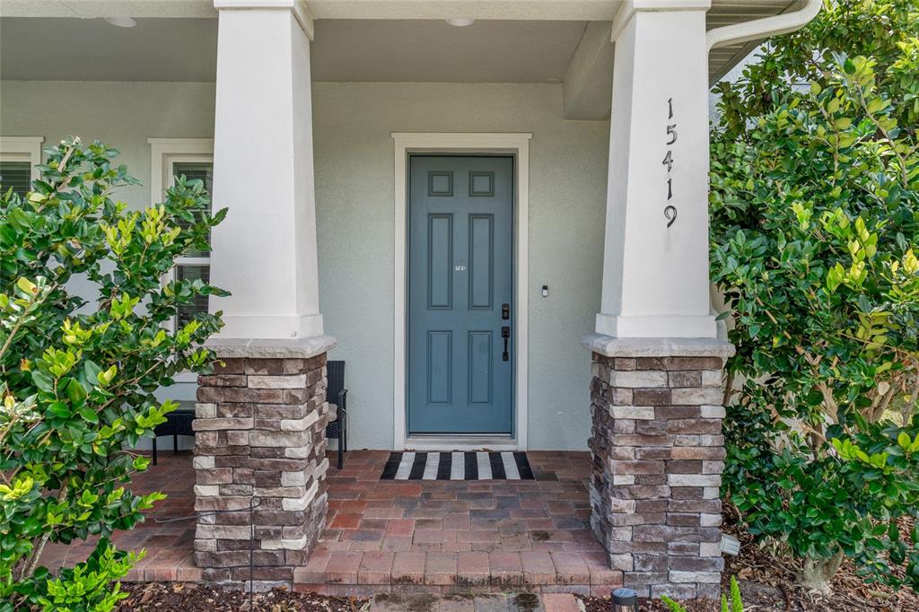 The front entrance features a blue door, stone-based columns, and a brick porch — 15419 UGLIS ALLEY, WINTER GARDEN, FL