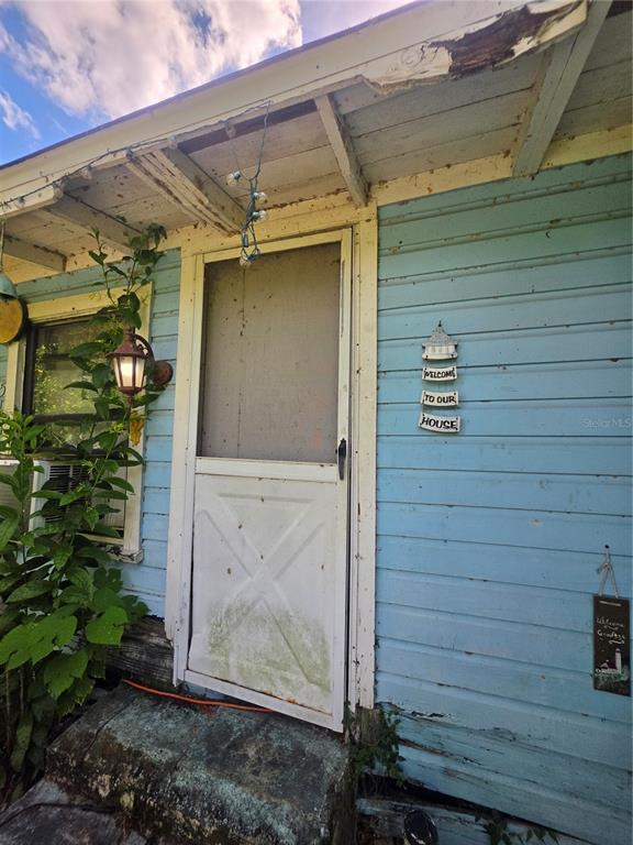 A weathered light blue house exterior features a screen door, a lantern, and welcome signs — 515 ELLA AVENUE, INVERNESS, FL