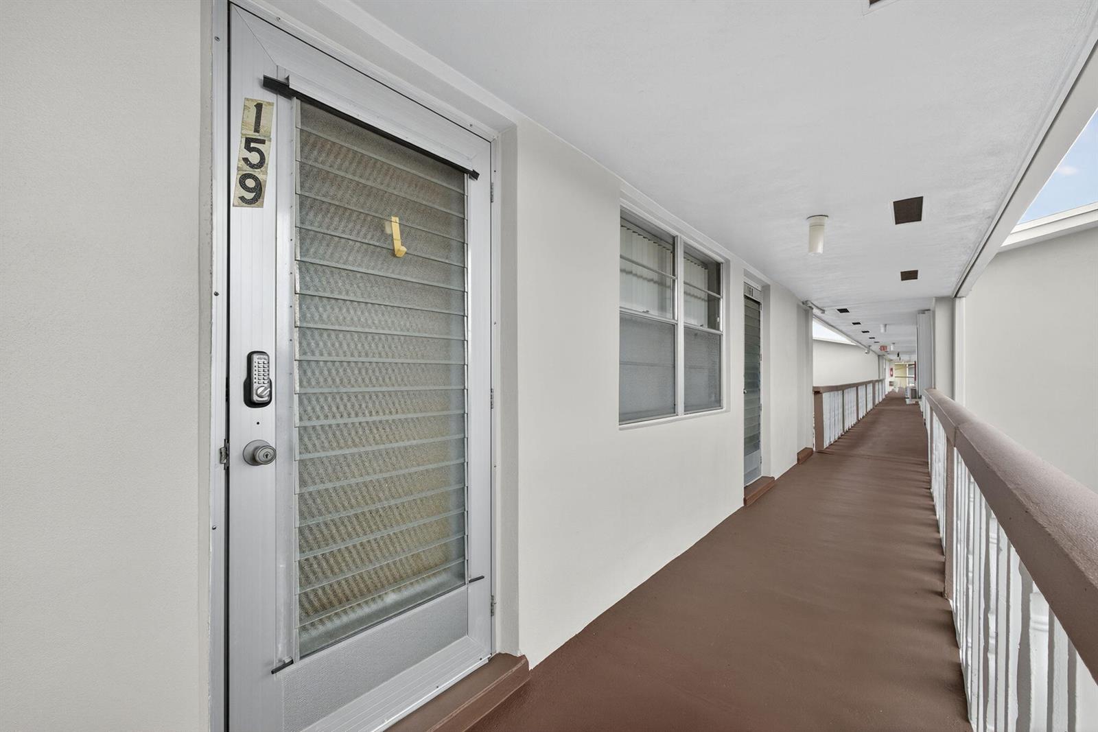 An exterior view of an apartment building hallway with a numbered door and railing — 159 Easthampton G, West Palm Beach FL 33417, WEST PALM BEACH, FL