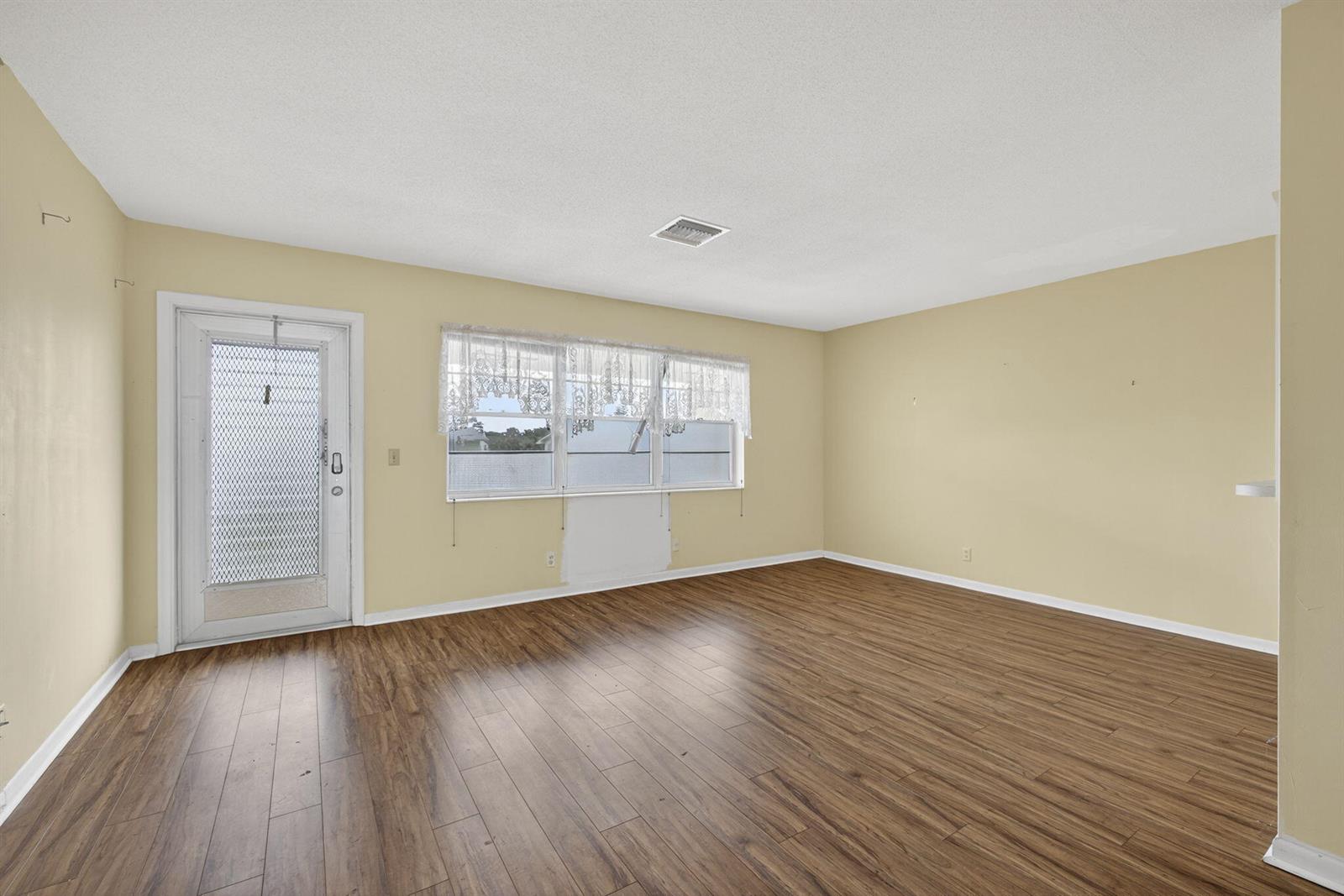 An empty room features light yellow walls, wood-look flooring, a white door, and windows — 159 Easthampton G, West Palm Beach FL 33417, WEST PALM BEACH, FL