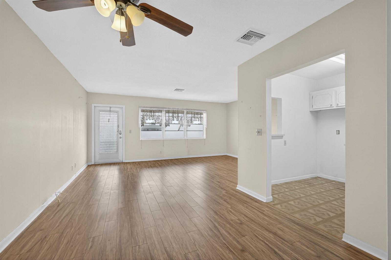 An empty living room with wood-look flooring, a ceiling fan, and an adjacent kitchen area — 159 Easthampton G, West Palm Beach FL 33417, WEST PALM BEACH, FL
