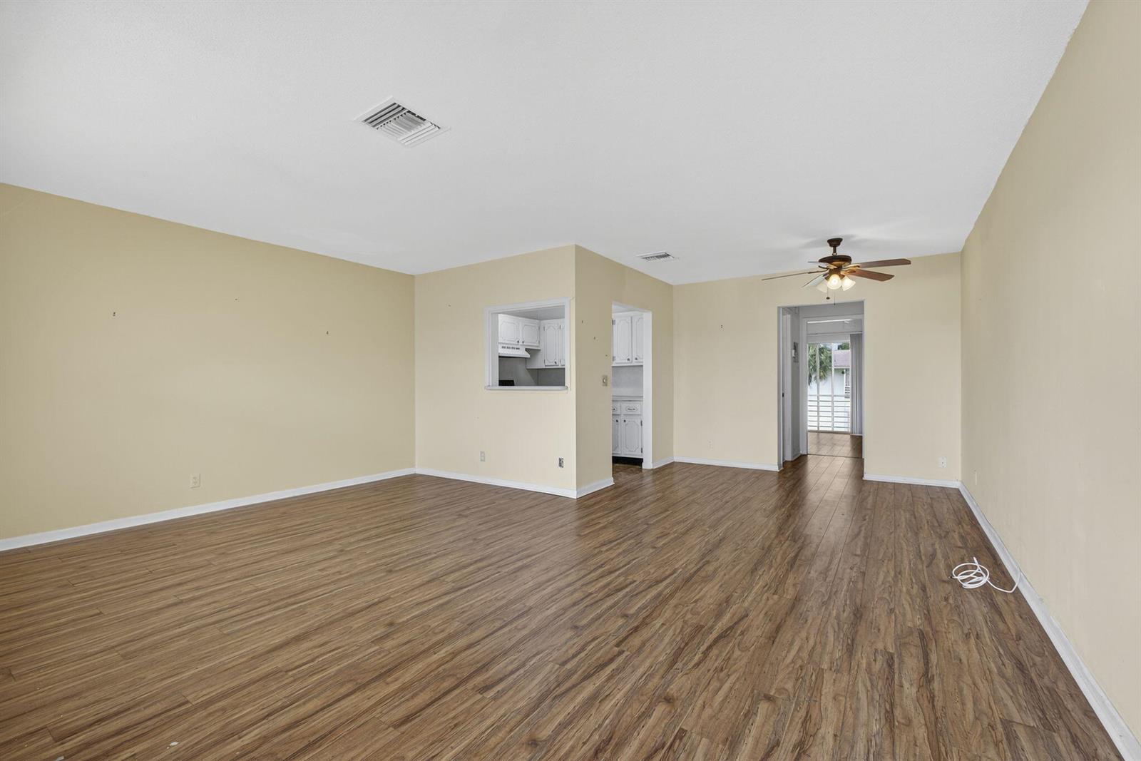 An empty living room features light-colored walls, wood-look flooring, a ceiling fan, and a pass-through window — 159 Easthampton G, West Palm Beach FL 33417, WEST PALM BEACH, FL