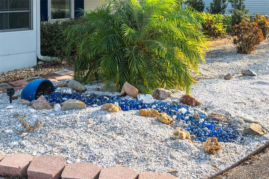 A landscaped yard features a decorative blue glass rock stream flowing from a blue pot — 7040 TAMARIND DRIVE, LAKE WALES, FL