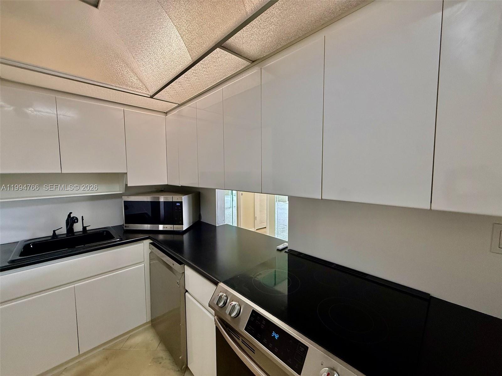 A kitchen features white cabinets, black countertops, stainless steel appliances, and a black sink — 500 Three Islands Blvd # 314, Hallandale Beach FL 33009, HALLANDALE BEACH, FL
