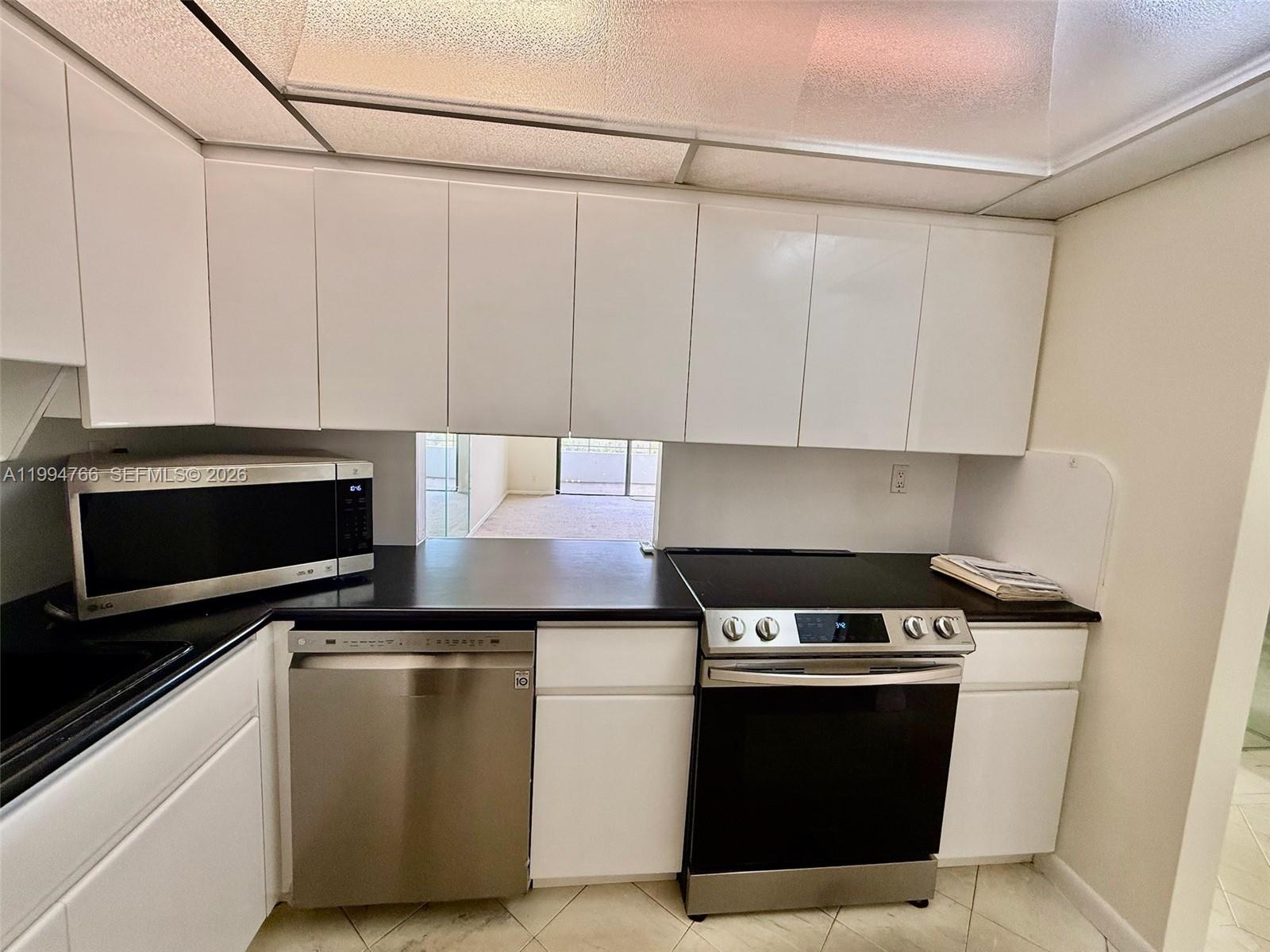 A kitchen features white cabinets, black countertops, stainless steel appliances, and a pass-through window — 500 Three Islands Blvd # 314, Hallandale Beach FL 33009, HALLANDALE BEACH, FL