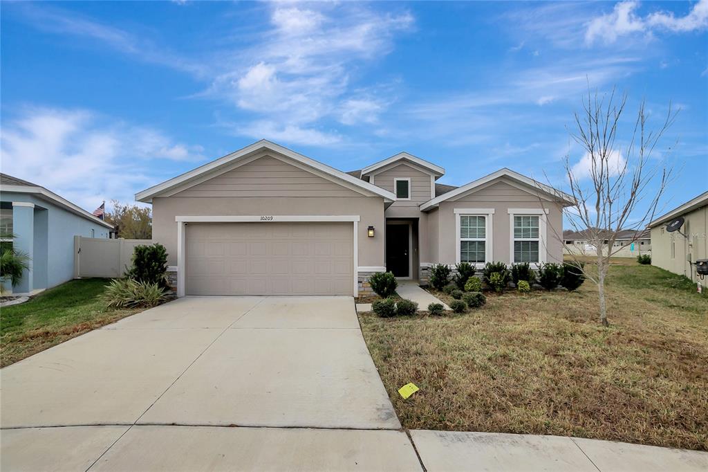 A single-story suburban house with a beige exterior, two-car garage, and a concrete driveway — 10209 AGAVE COURT, LAND O LAKES, FL