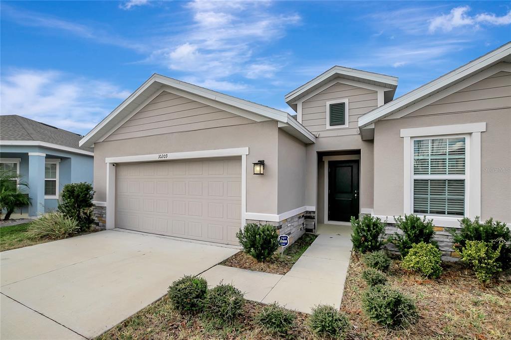A beige single-story house features a two-car garage, stone accents, and a front entryway — 10209 AGAVE COURT, LAND O LAKES, FL