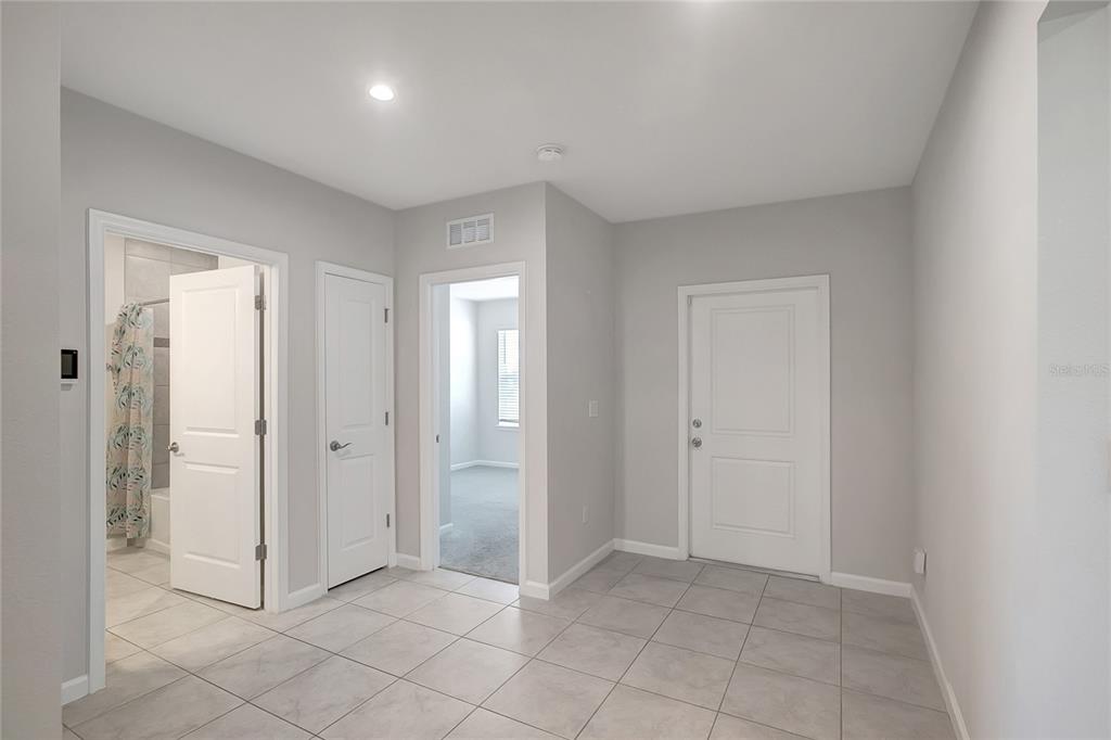 A tiled entryway features three white doors, a hallway leading to a bedroom, and light-gray walls — 10209 AGAVE COURT, LAND O LAKES, FL