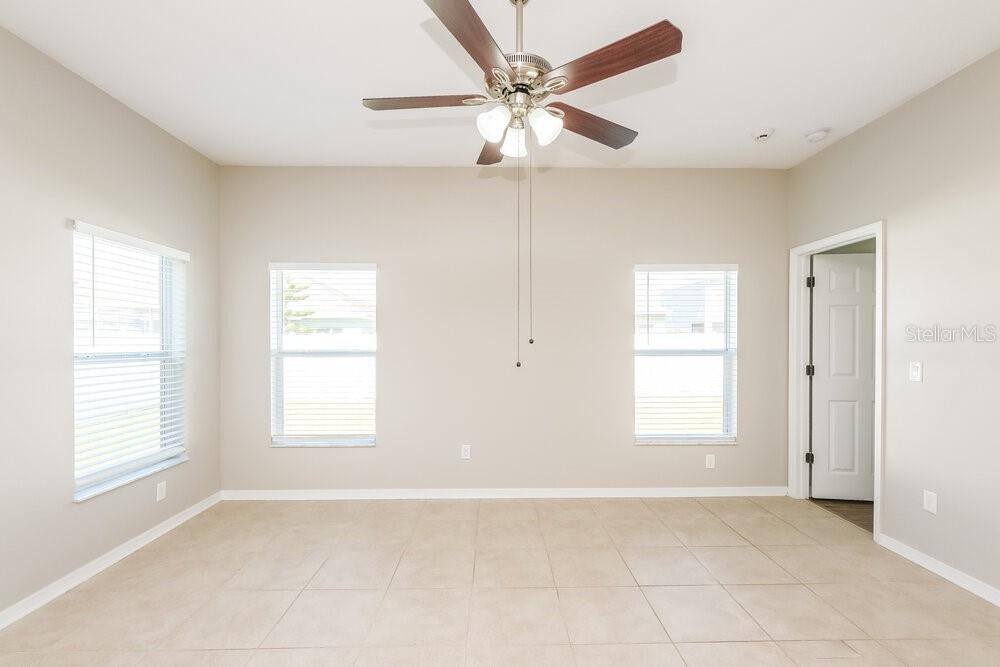 An empty room with beige walls, tile flooring, three windows, and a ceiling fan — 1807 BONITA BLUFF COURT, RUSKIN, FL