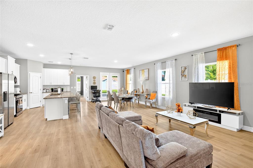An open-concept living room and kitchen featuring light wood flooring, white cabinetry, and a sectional — 14055 SW 30TH TERRACE ROAD, OCALA, FL