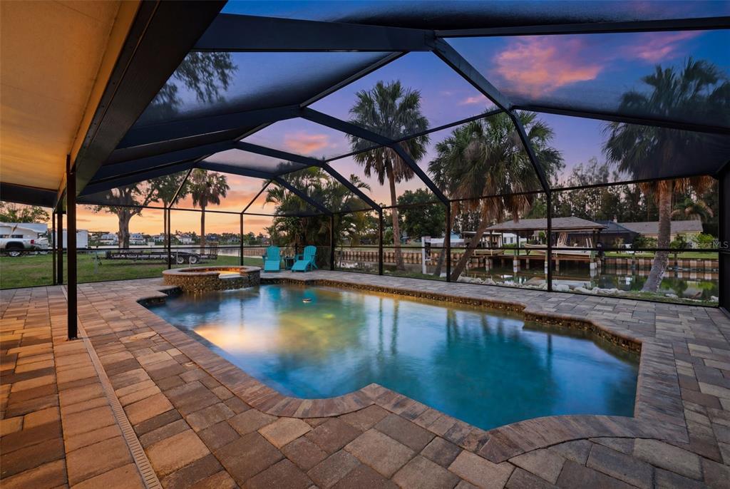 A screened-in pool and hot tub on a stone patio overlooking a canal at sunset — 9910 PENINSULAR DRIVE, GIBSONTON, FL