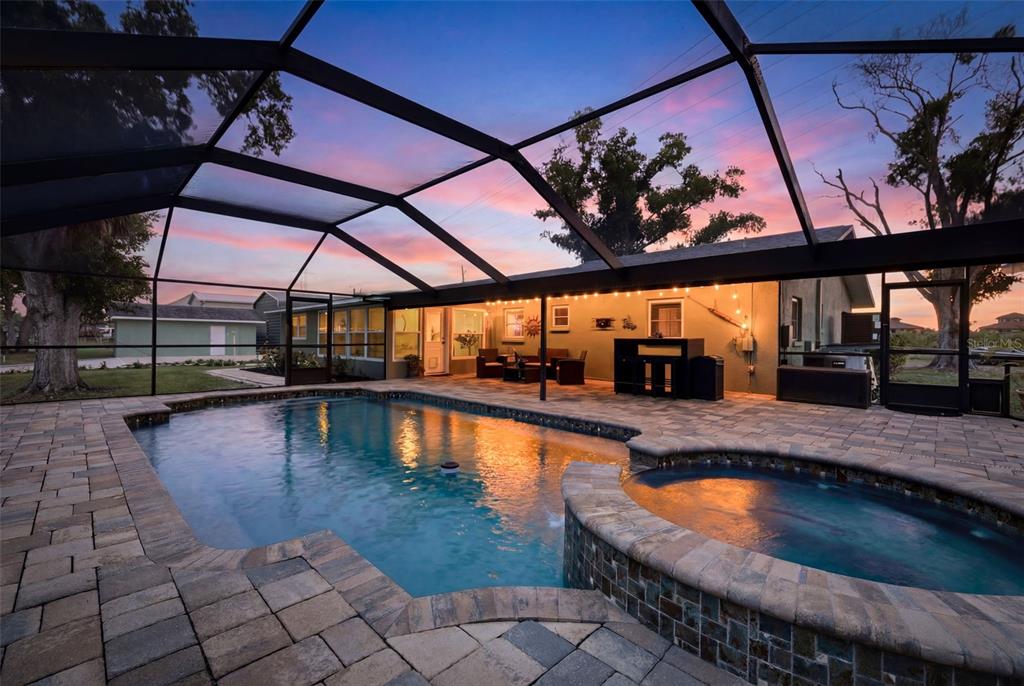 A screened-in patio features a swimming pool, a raised spa, and paved decking at sunset — 9910 PENINSULAR DRIVE, GIBSONTON, FL
