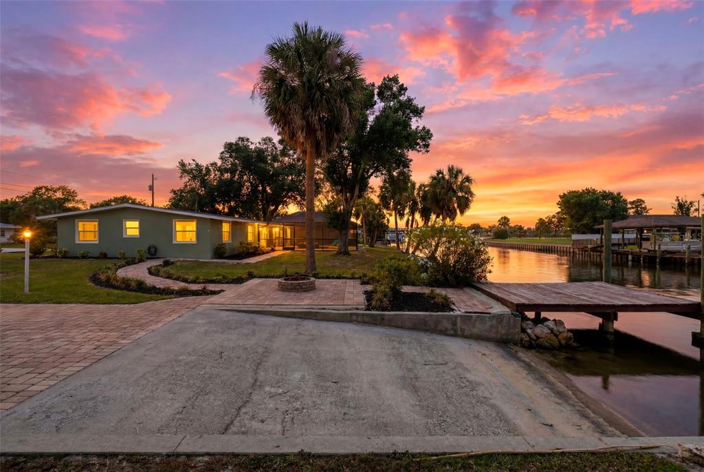 A waterfront house with a boat ramp, wooden dock, and fire pit at sunset — 9910 PENINSULAR DRIVE, GIBSONTON, FL