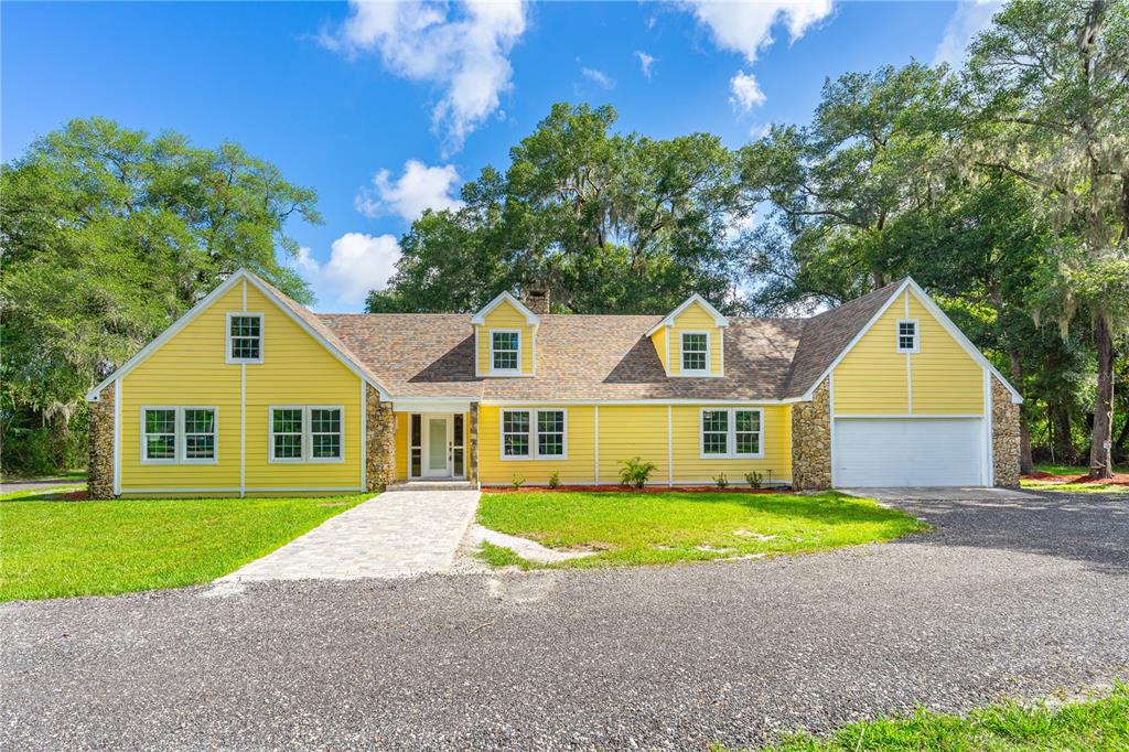 A yellow, one-story house with stone accents, a gravel driveway, and a paved walkway — 475 E WISCONSIN AVENUE, ORANGE CITY, FL