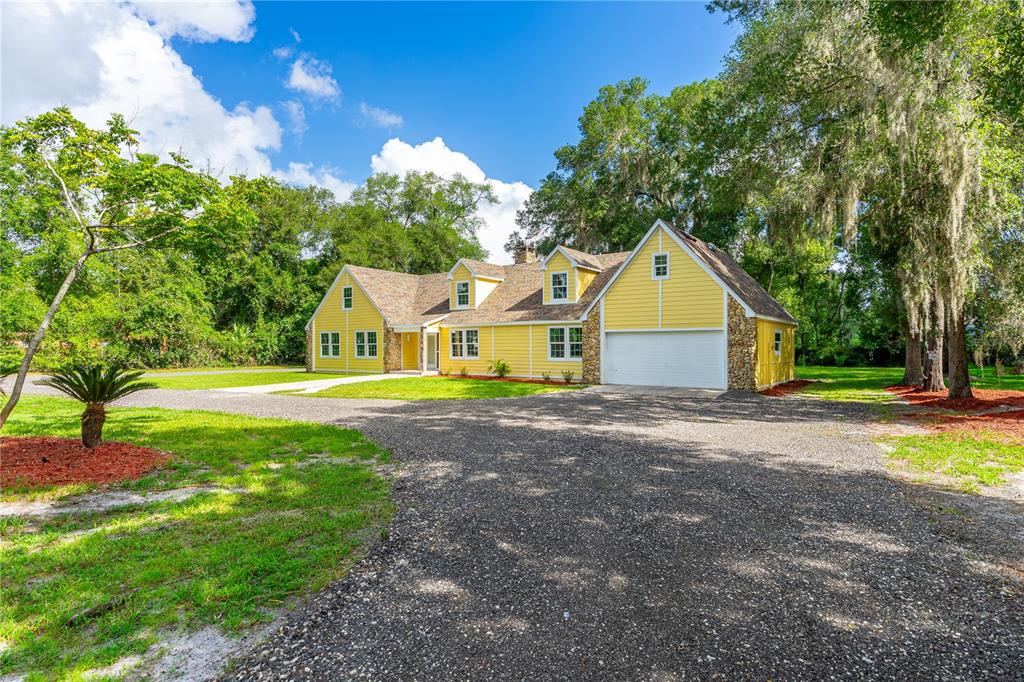 A yellow house with stone accents and a gravel driveway sits on a grassy lot — 475 E WISCONSIN AVENUE, ORANGE CITY, FL