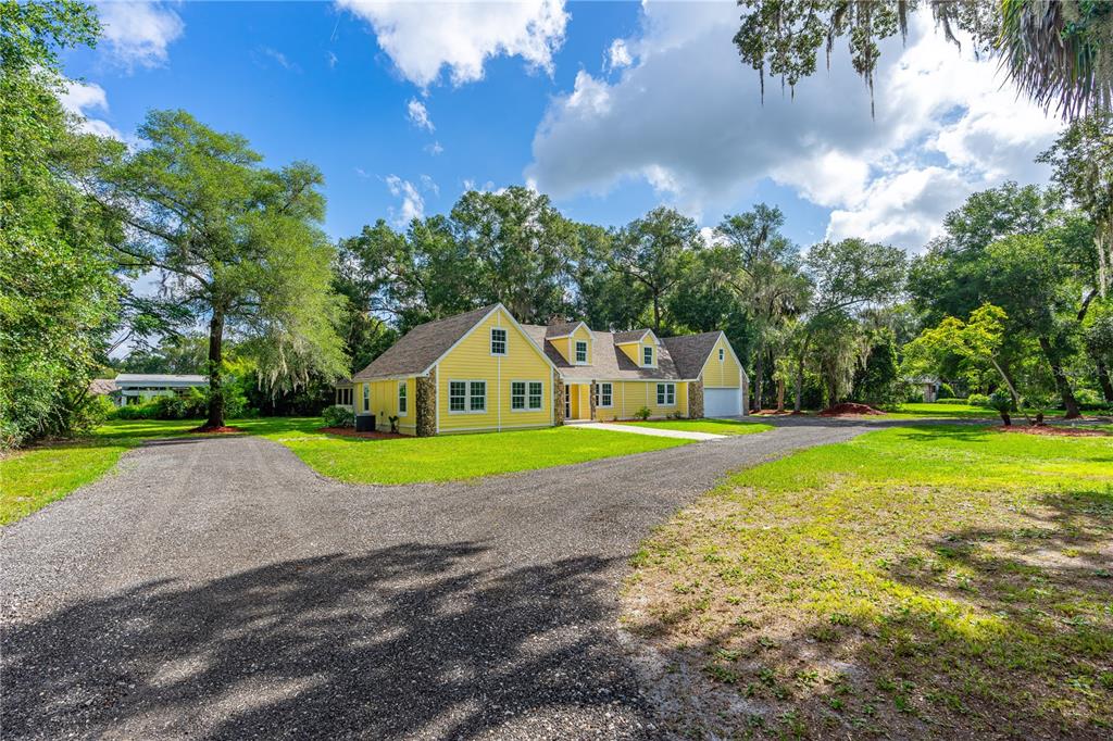 A yellow house with a stone-accented exterior sits at the end of a gravel driveway — 475 E WISCONSIN AVENUE, ORANGE CITY, FL