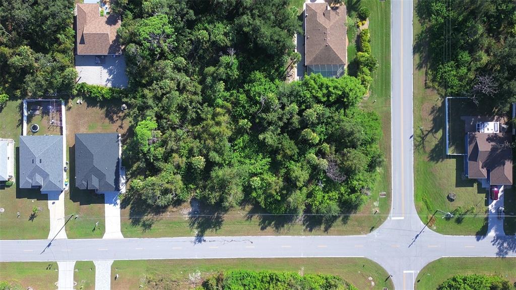 An aerial view shows a wooded vacant lot situated between several residential houses and roads — 197 COUGAR WAY, ROTONDA WEST, FL