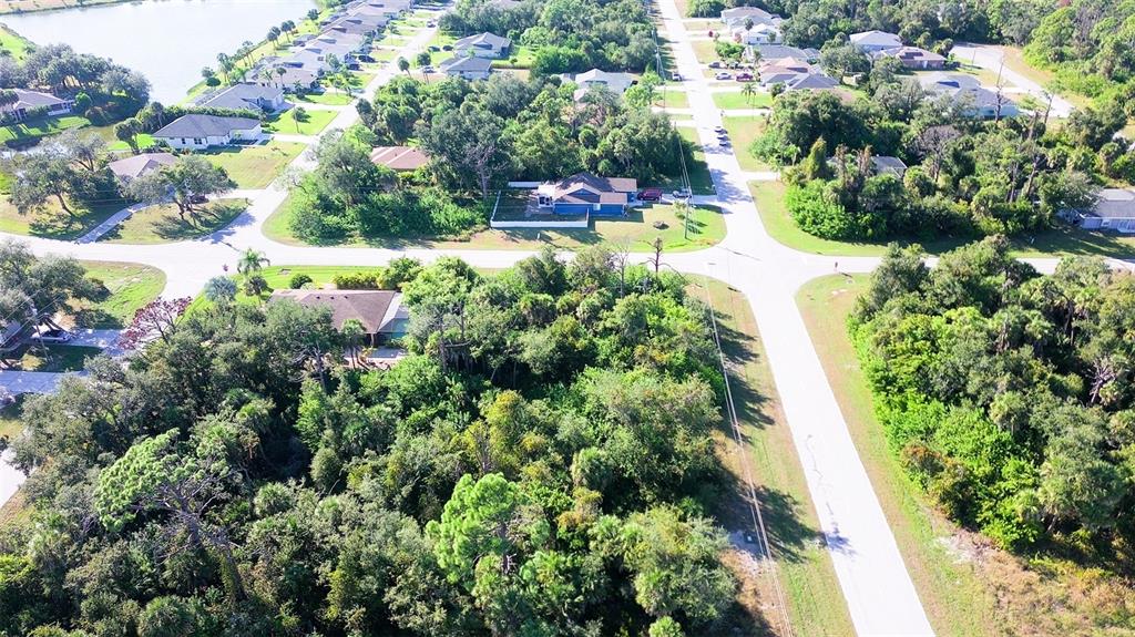 An aerial view shows a suburban neighborhood with houses, dense trees, and paved roads — 197 COUGAR WAY, ROTONDA WEST, FL