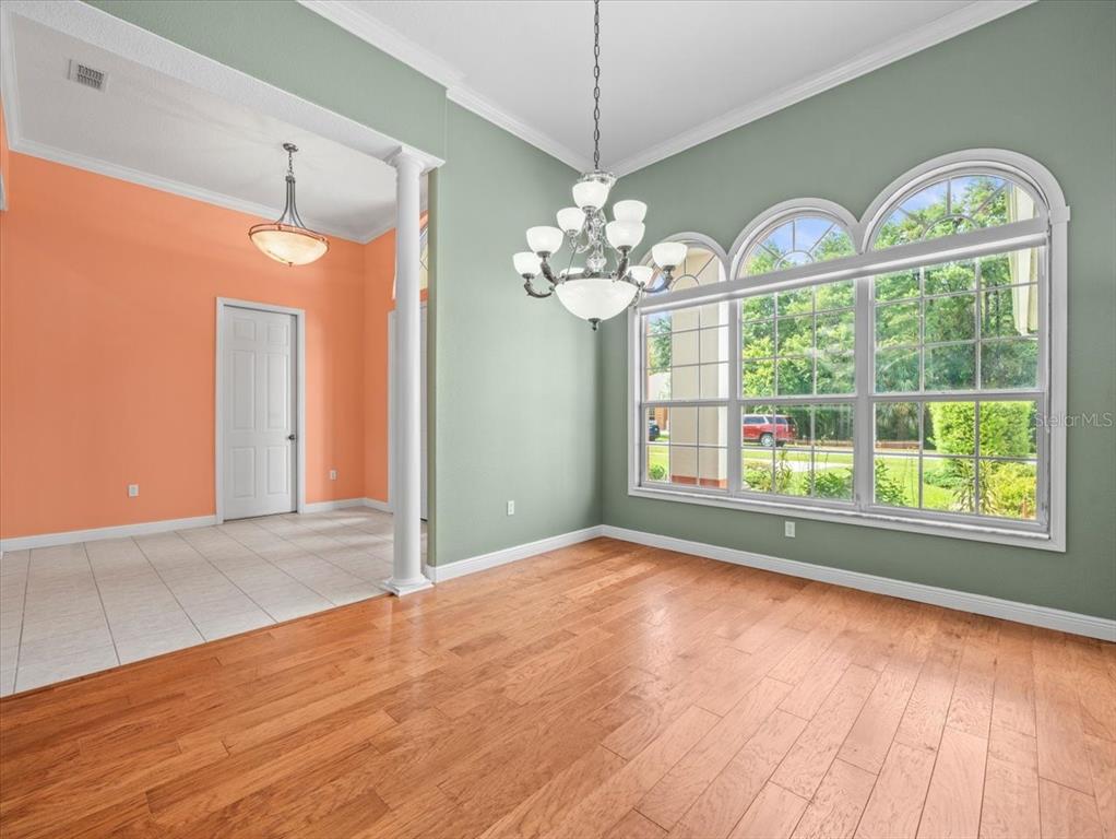 A dining room features sage green walls, hardwood floors, a chandelier, and large arched windows — 8698 MISSISSIPPI RUN, WEEKI WACHEE, FL