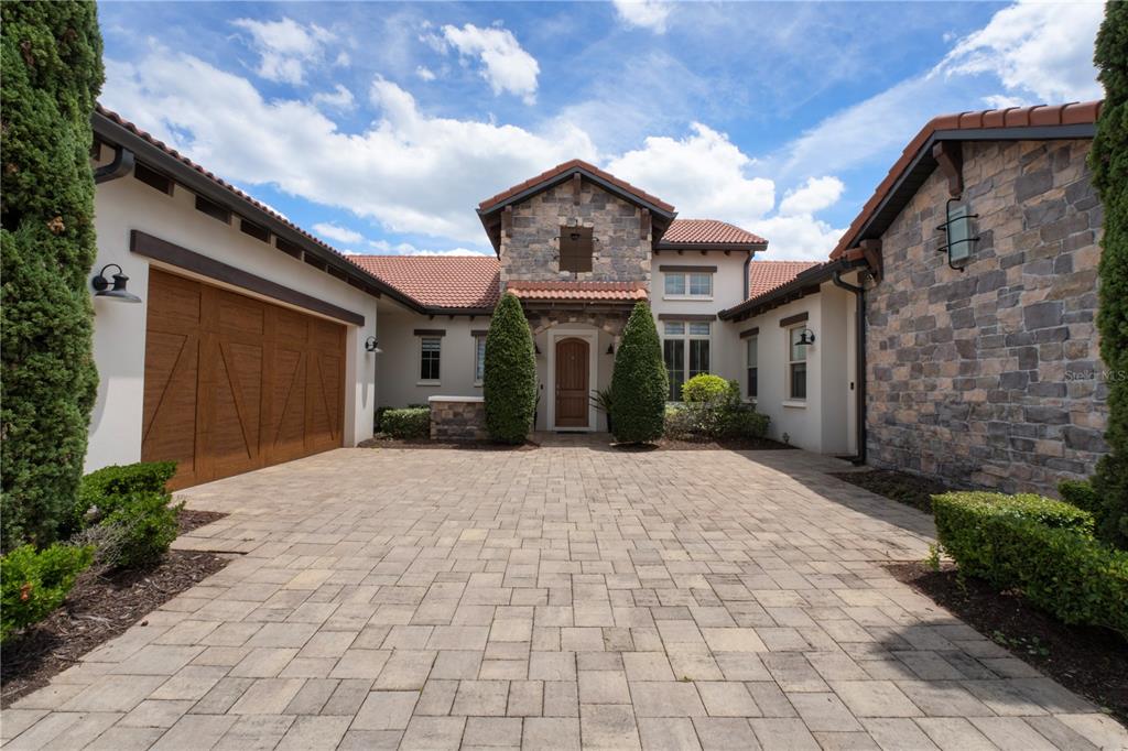A stone and stucco house exterior with a paver driveway and a wooden garage door — 15686 PANTHER LAKE DRIVE, WINTER GARDEN, FL