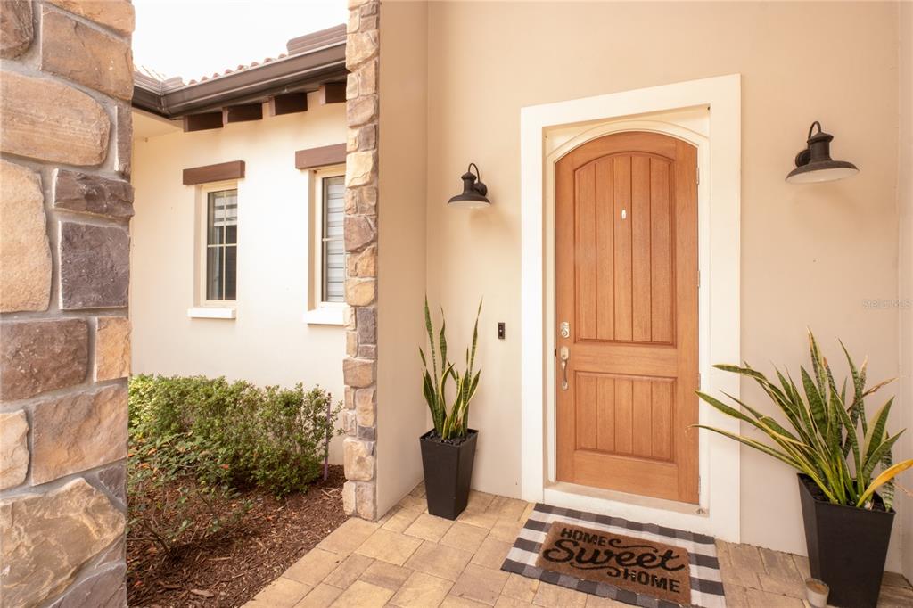 An arched wooden front door is flanked by two potted snake plants and wall sconces — 15686 PANTHER LAKE DRIVE, WINTER GARDEN, FL