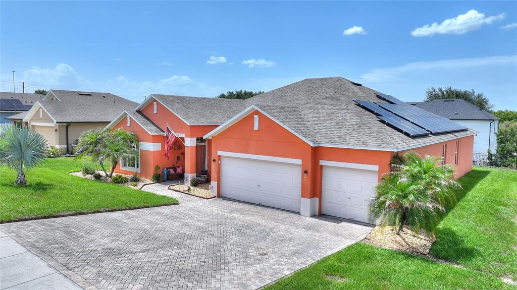 An orange single-story house with a paver driveway, two-car garage, and roof-mounted solar panels — 212 BROOKSHIRE DRIVE, LAKE WALES, FL