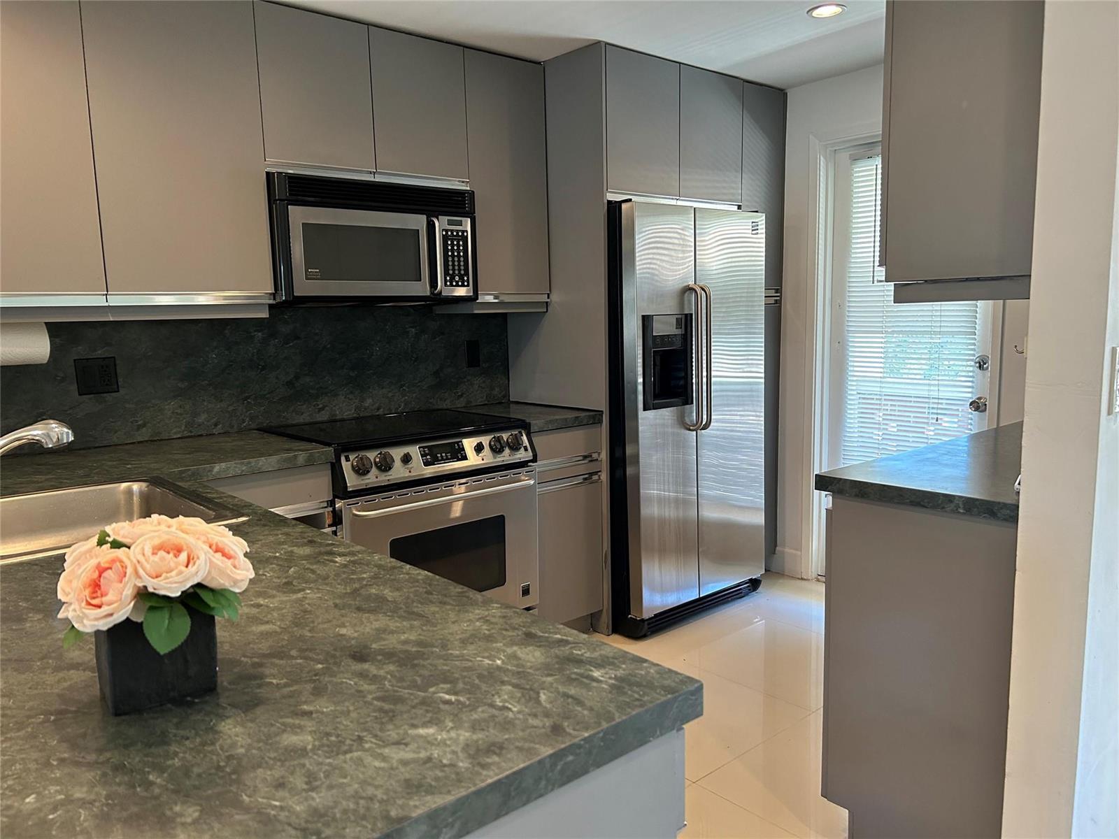 A modern kitchen features gray cabinets, stainless steel appliances, and dark green stone countertops — 2800 NE 14th St Causeway # 207, Pompano Beach FL 33062, POMPANO BEACH, FL