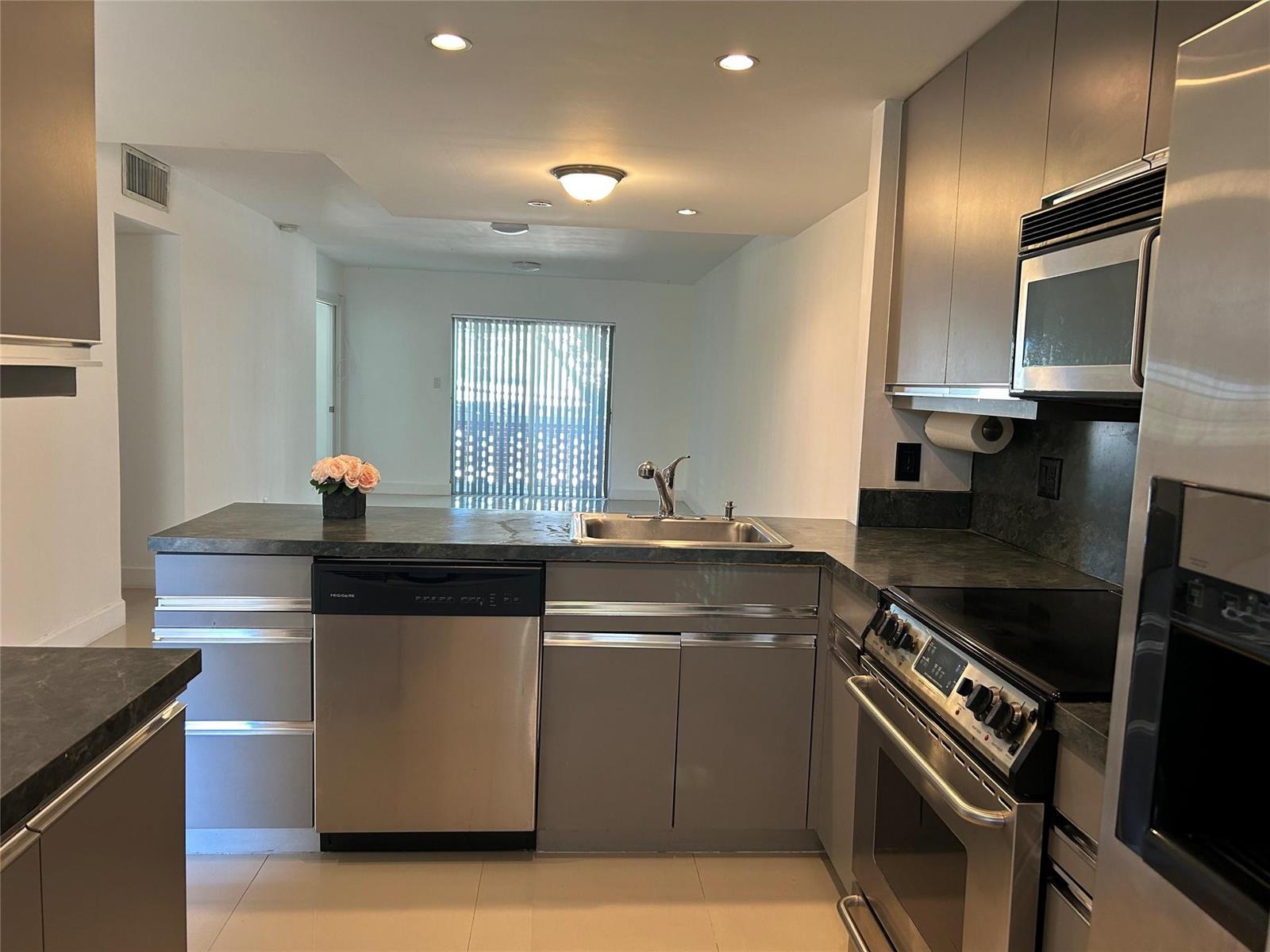 A kitchen with grey cabinets, stainless steel appliances, and a dark countertop overlooks a room — 2800 NE 14th St Causeway # 207, Pompano Beach FL 33062, POMPANO BEACH, FL