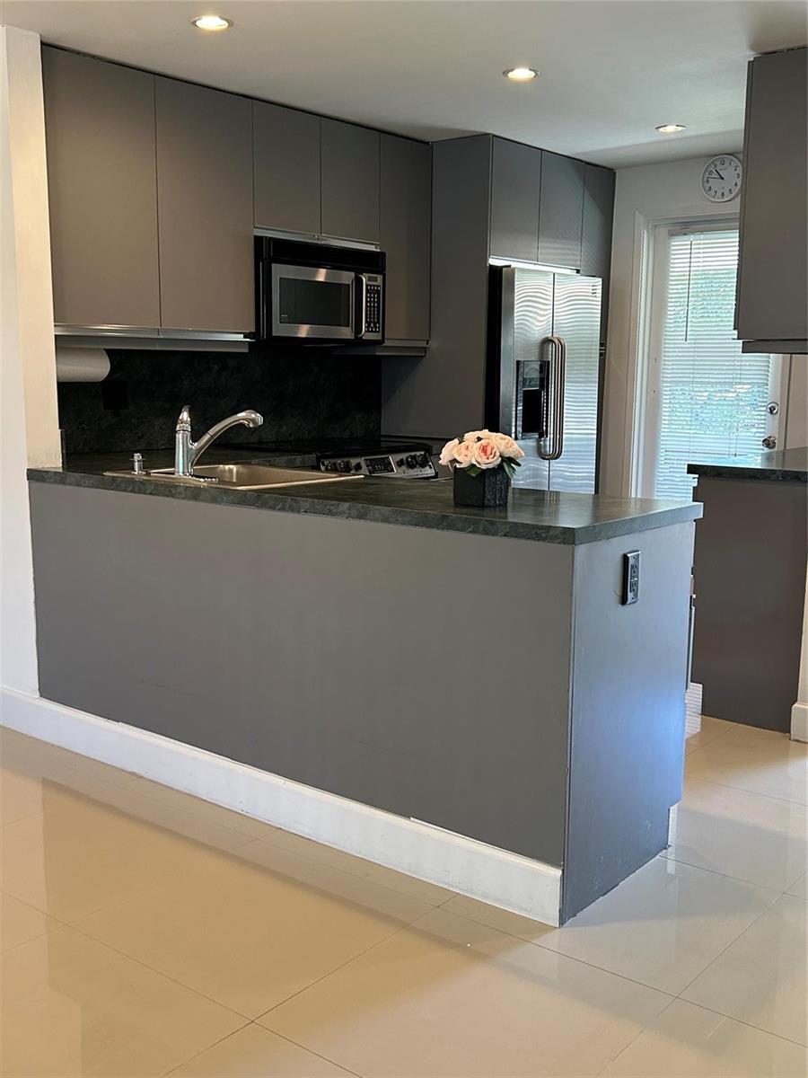 A kitchen features gray cabinets, a dark countertop, a stainless steel refrigerator, and tile flooring — 2800 NE 14th St Causeway # 207, Pompano Beach FL 33062, POMPANO BEACH, FL