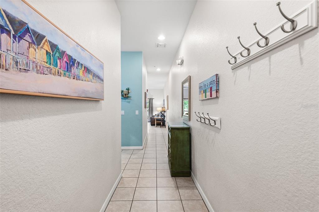 A hallway with tiled floors, wall-mounted coat hooks, and a painting of beach huts — 402 LUCAYA LOOP, DAVENPORT, FL