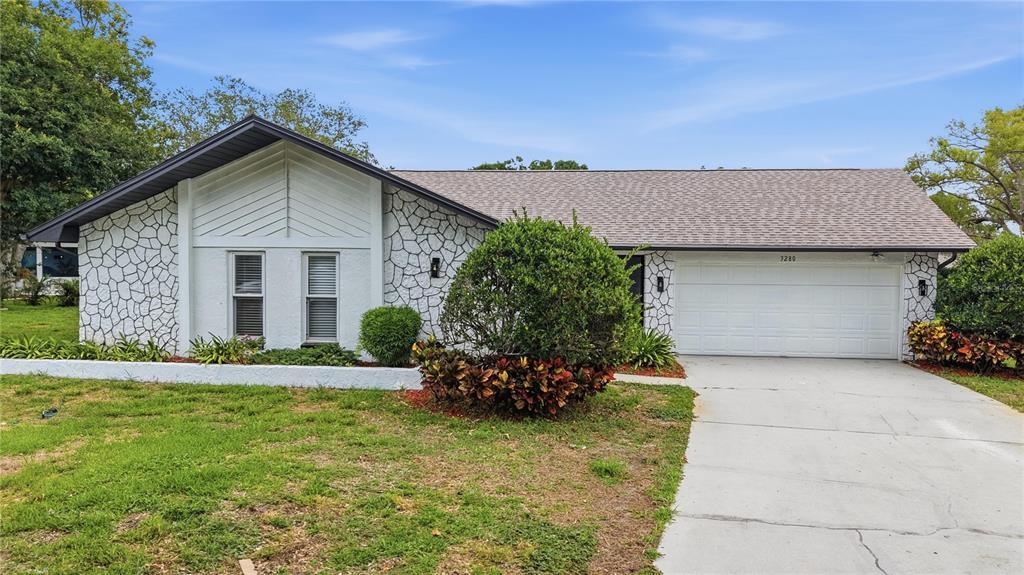 A single-story house features a stone-patterned facade, a two-car garage, and a front lawn — 3280 SKENE TERRACE, PALM HARBOR, FL
