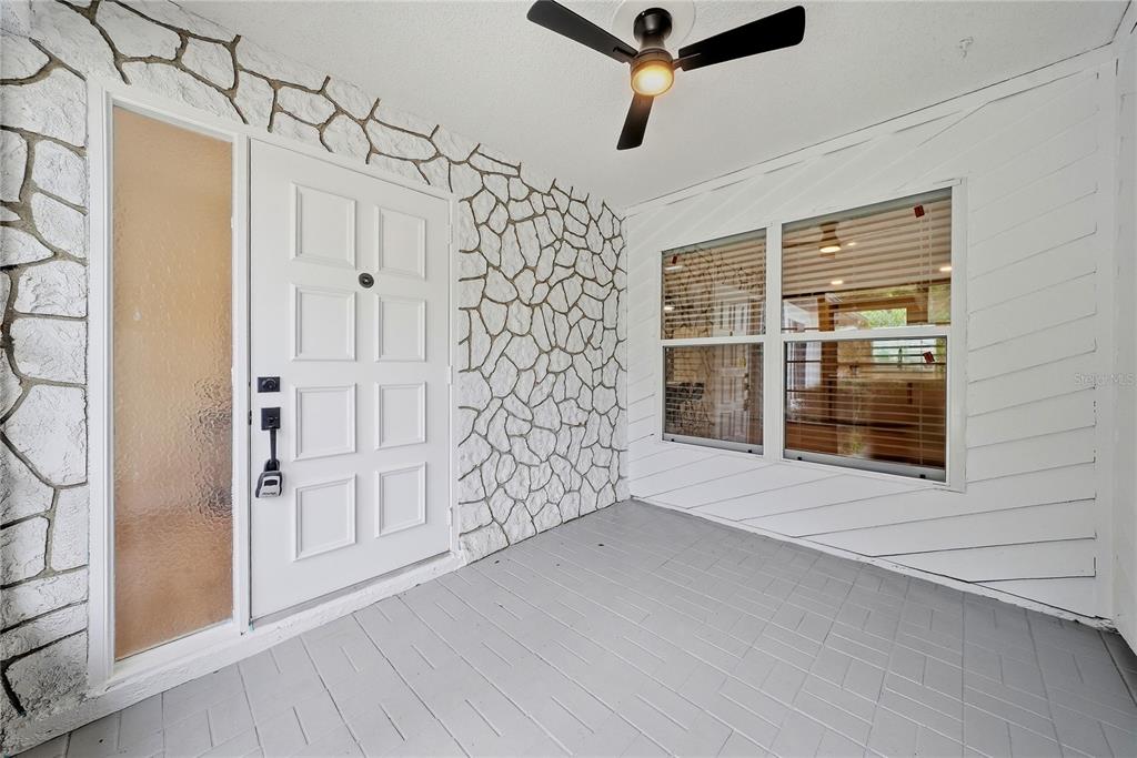 A covered porch features a white front door, stone-patterned walls, and a ceiling fan — 3280 SKENE TERRACE, PALM HARBOR, FL