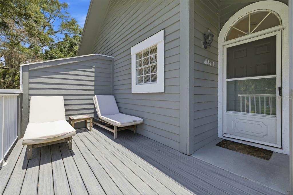 A gray wooden deck features two lounge chairs and a white door with an arched window — 11844 SKYLAKE PLACE, TAMPA, FL