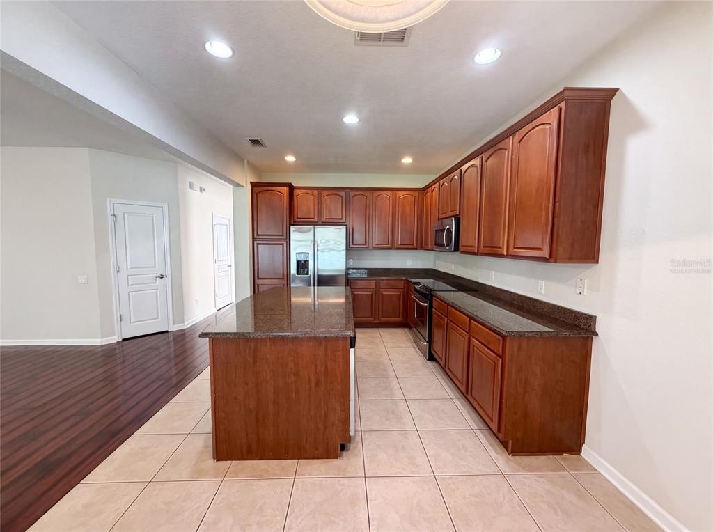 A kitchen features dark wood cabinets, granite countertops, a center island, and tile flooring — 13228 ROSKIN LANE, WINDERMERE, FL